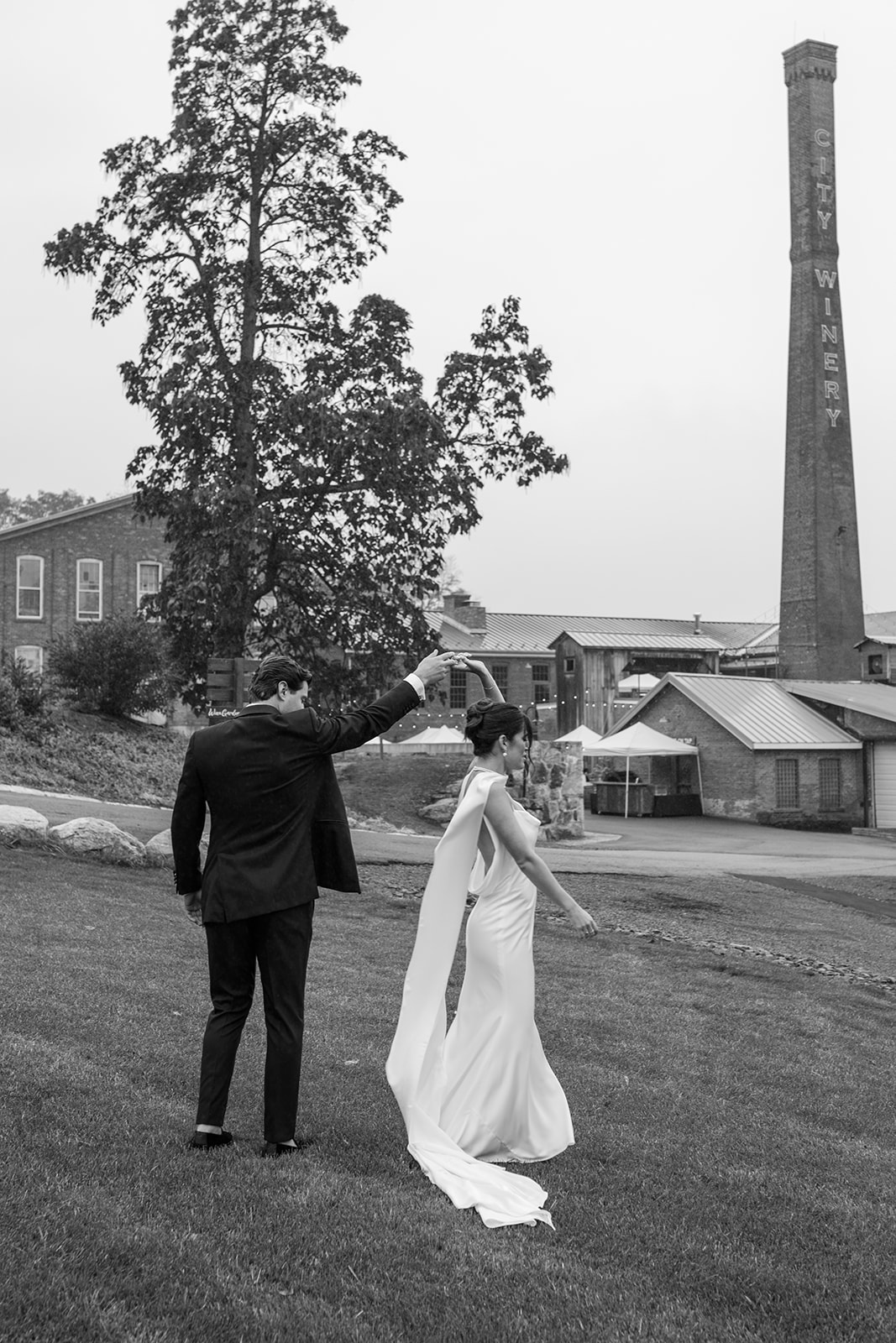 Groom twirling his bride on the lawn beneath the City Winery smokestack in Montgomery, NY, black and white